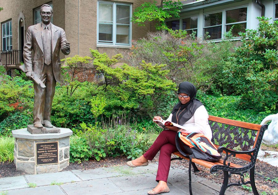 Student sits studying on campus bench beside Walter R. Garrison statue.